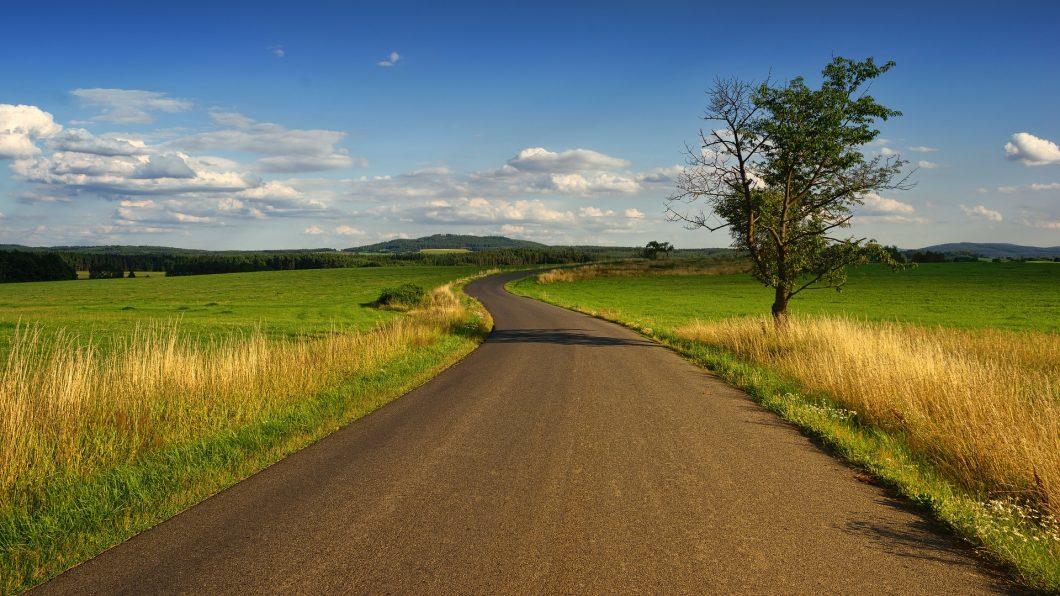 A landscape photo with a road that extends toward hills on the horizon.